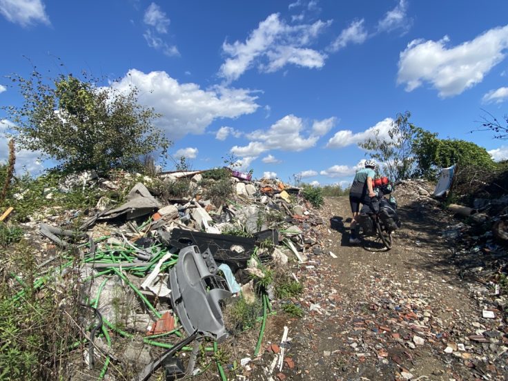 Radfahrer schiebt bepacktes Gravelbike über eine Müllkippe