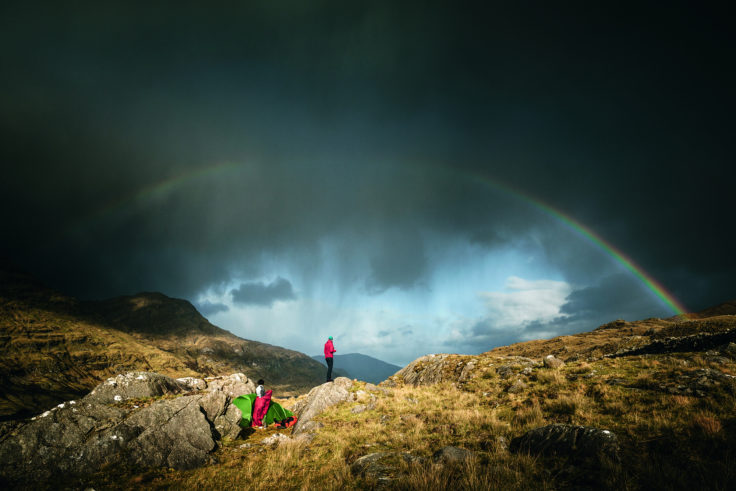 Zwei Personen und Zelt in irischer Landschaft mit Regenbogen am Himmel.