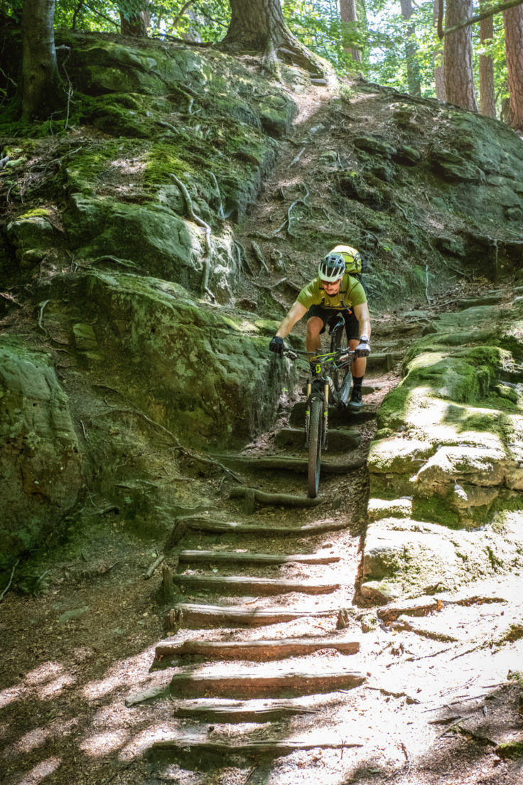 Mountainbiker fährt Stufen neben Felsen im Wald hinunter.