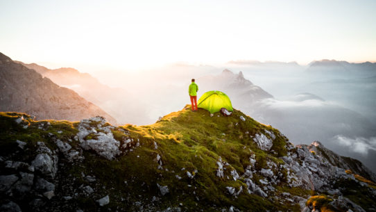 Wanderer mit Zelt bei Sonnenaufgang in den Alpen