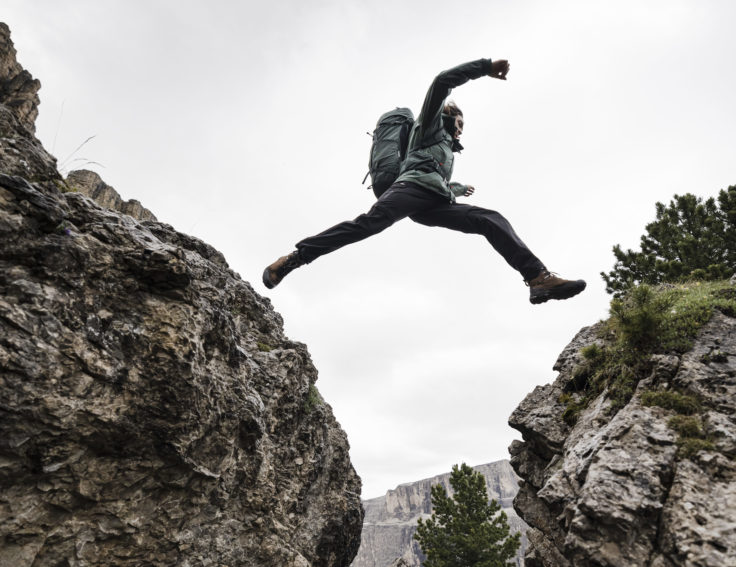 Wanderer springt über Felsspalt mit elastischer Wanderhose